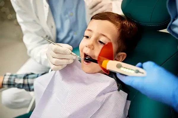 A child receiving a dental sealant application using a curing light, assisted by a dentist at Brush & Floss Dental Center in Stratford, CT
