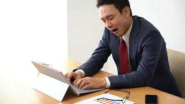 Sleep-deprived businessman yawning at his desk, appearing drowsy and unproductive, due to sleep apnea.